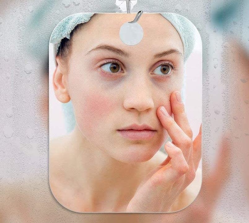 A person inspects their face in the fogless mirror that hangs on a fogged-up mirror in the bathroom