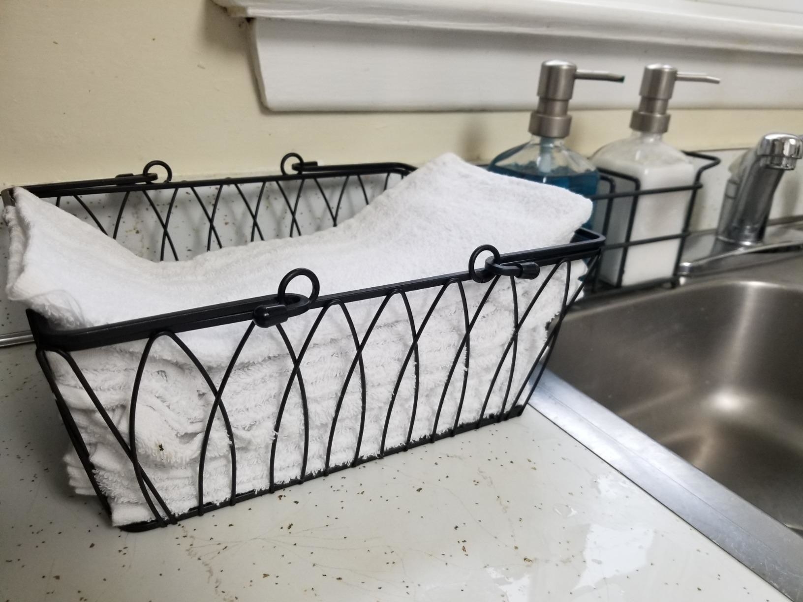 Reviewer pic of the wire basket with handles filled with hand towels next to a sink