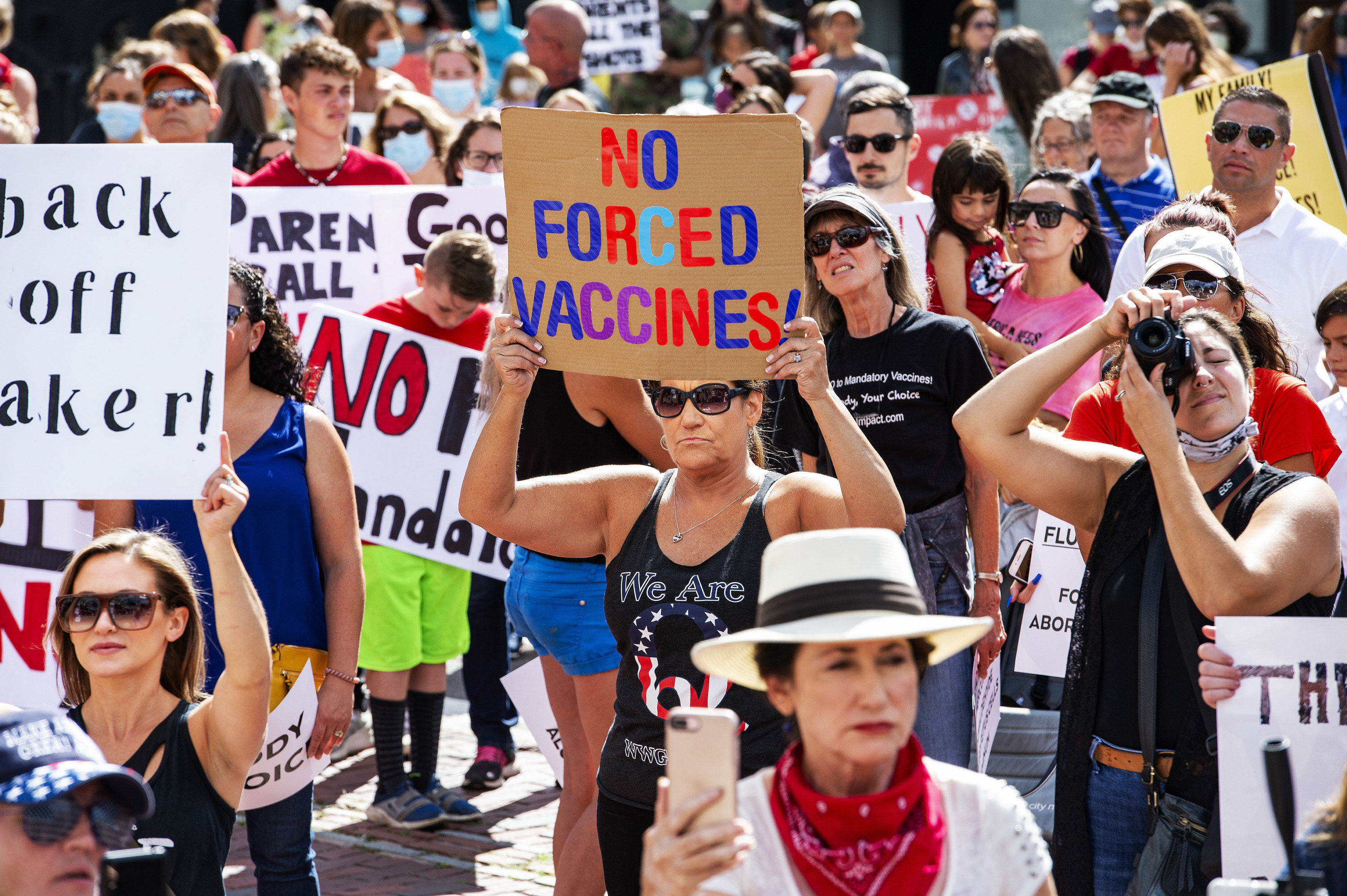 A crowd of people is protesting, one sign says &quot;No forced vaccines&quot;