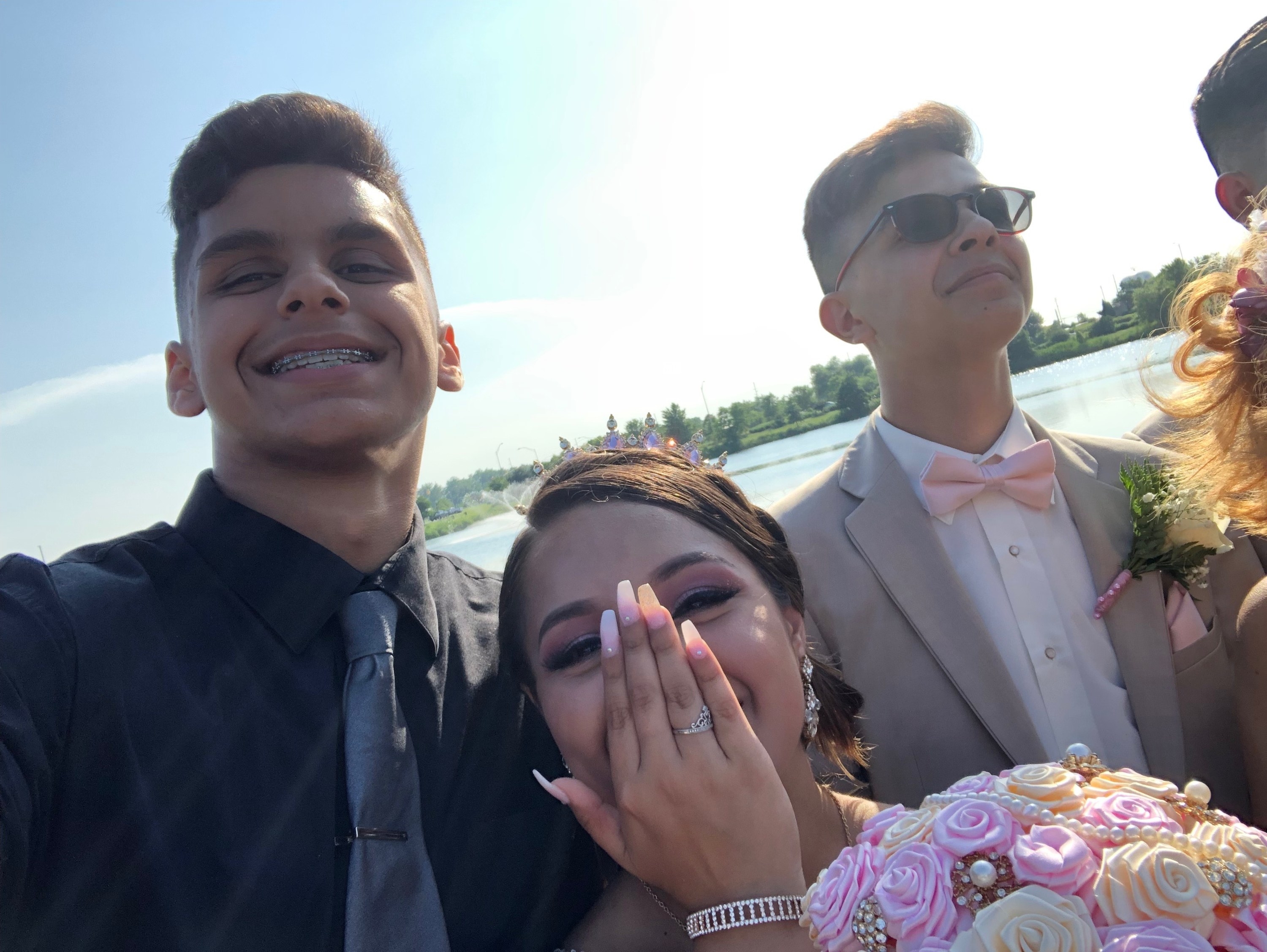 Noel wears a black shirt and gray tie, smiling with braces; next to him is Viviana, grinning and covering her mouth, holding a bouquet of flowers