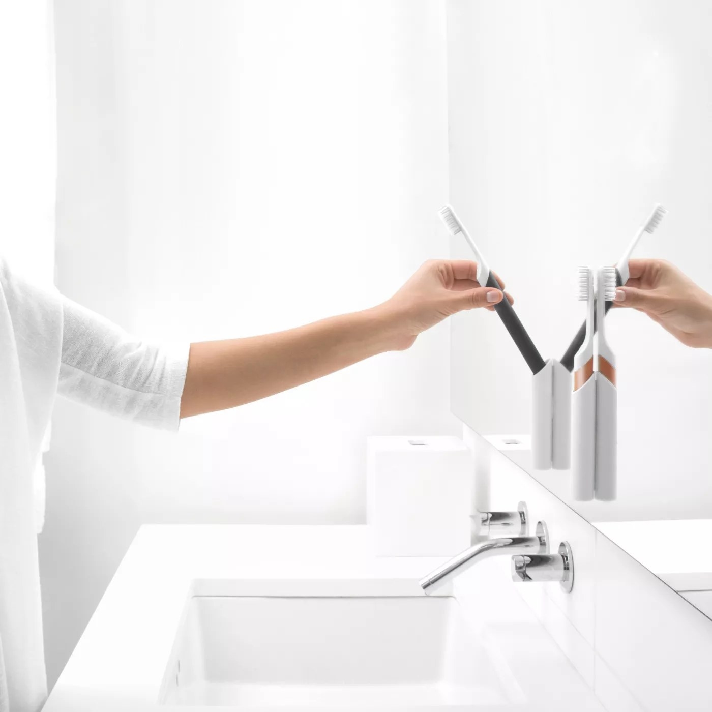 A model putting their toothbrush back in the holder attached to a mirror