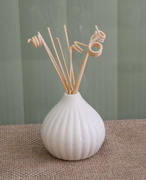 A white ceramic pot with reeds sticks