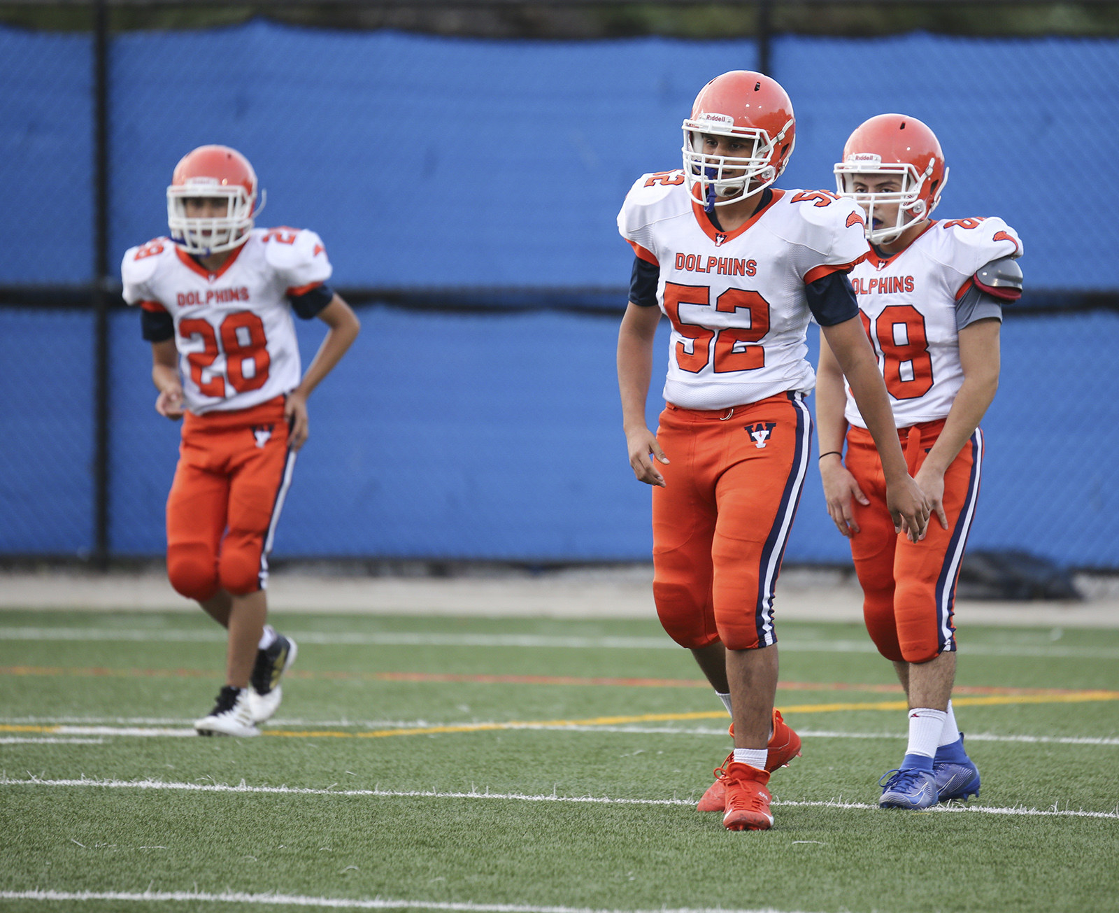 High school football players wear white-and-orange uniforms on the field