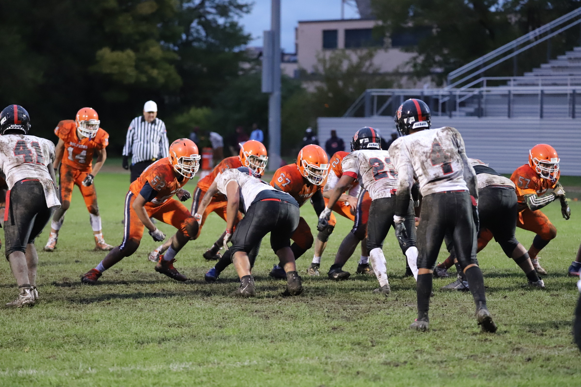 High school football players in orange and white uniforms play on a muddy field