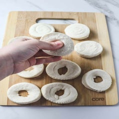 A hand pinching a hole in the center of a biscuit to make donuts.