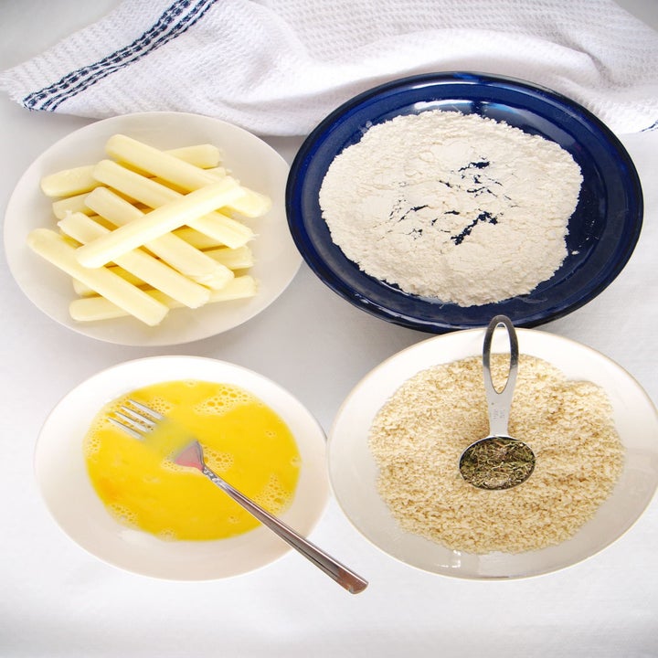 Cheese sticks and bowls containing egg, flour, and bread crumbs.