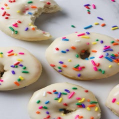 Four biscuit donuts topped with vanilla icing and rainbow sprinkles.