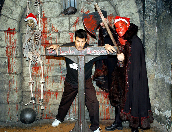 man in dungeon with man in devil costume holding an axe