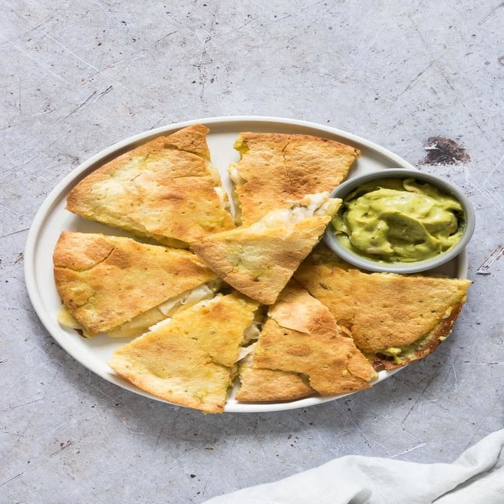 A sliced chicken and cheese quesadilla on a plate with a little bowl of guacamole.