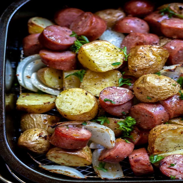 Sausage, peppers, and onion with fresh herbs in the air fryer basket.