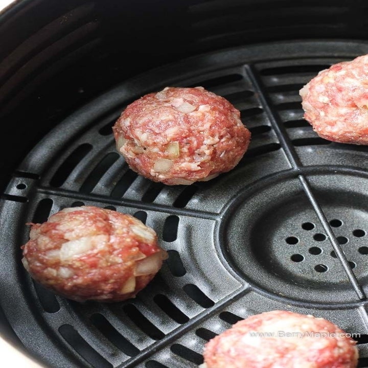 Four homemade meatballs cooking in the basket of an air fryer.