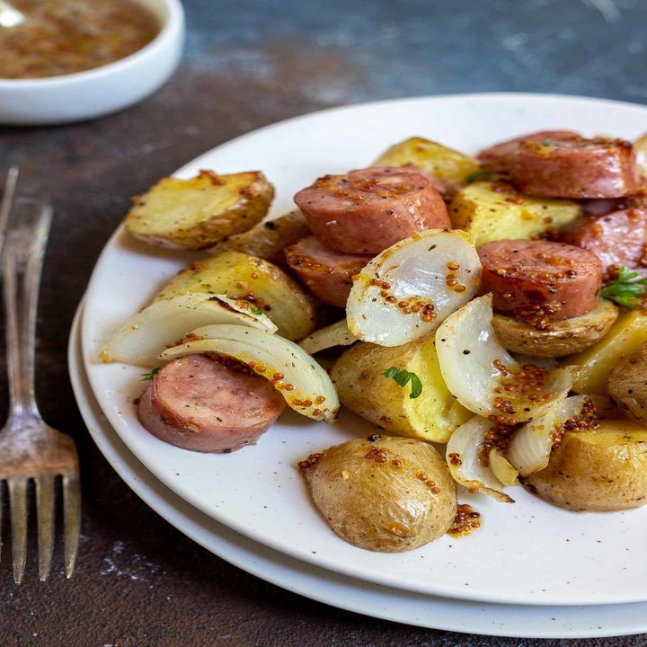 A dinner plate topped with chopped sausage, onions, and potato wedges in honey mustard.