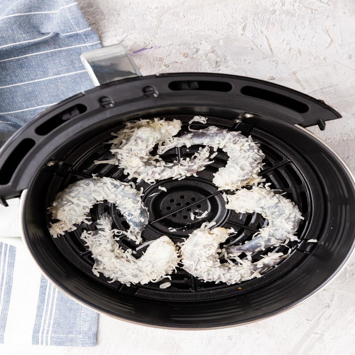 Six coconut coated shrimp cooking in the basket of an air fryer.