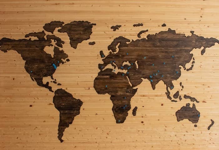 A wooden, flat map of the world carved into a wooden board, with blue pin stuck in various locations.