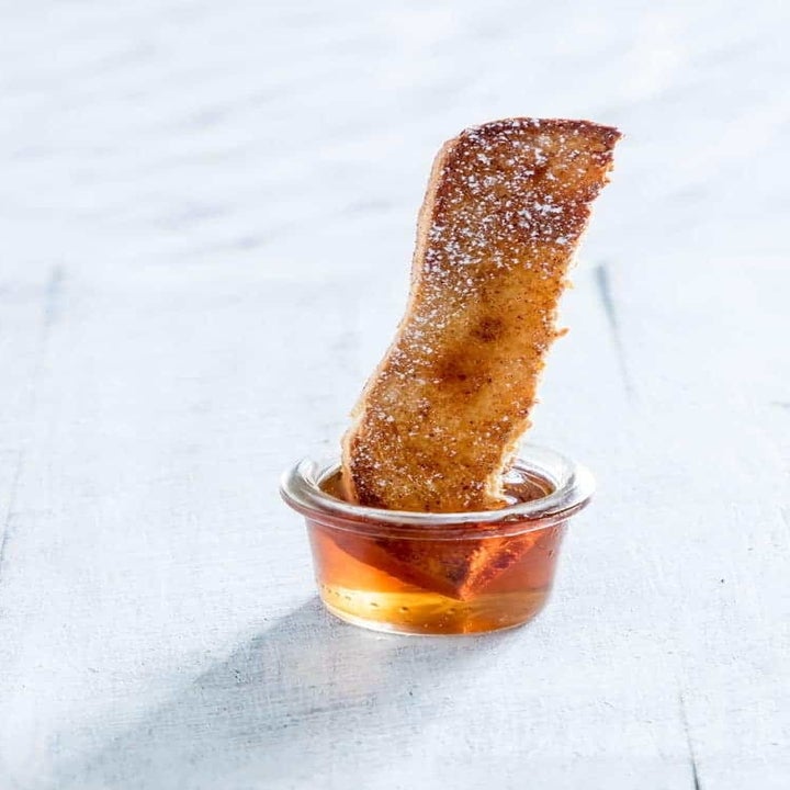 A single French toast stick being dipped into a bowl of maple syrup.