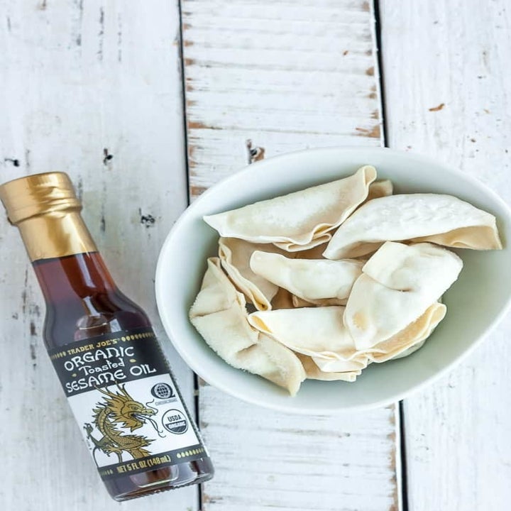 A bowl of frozen dumplings and a bottle of sesame oil.