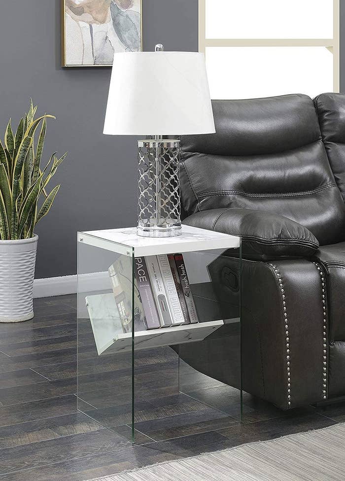 end table has glass sides with a marble top and a tilted marble shelf inside with books on it