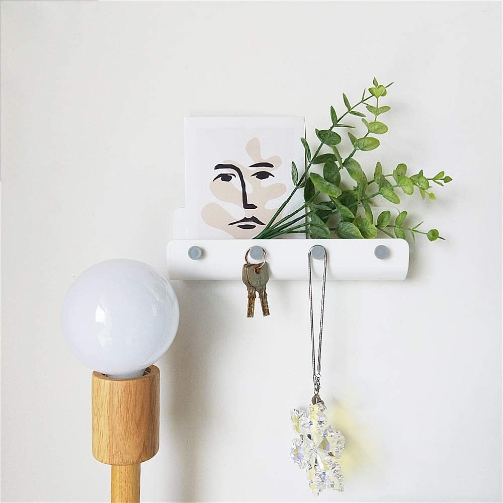 A white wall organizer with four hooks for keys 