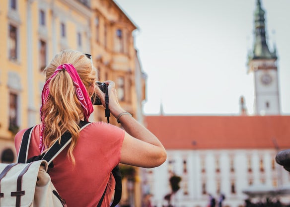 A woman faces away as she takes a photo of a European style building with a camera