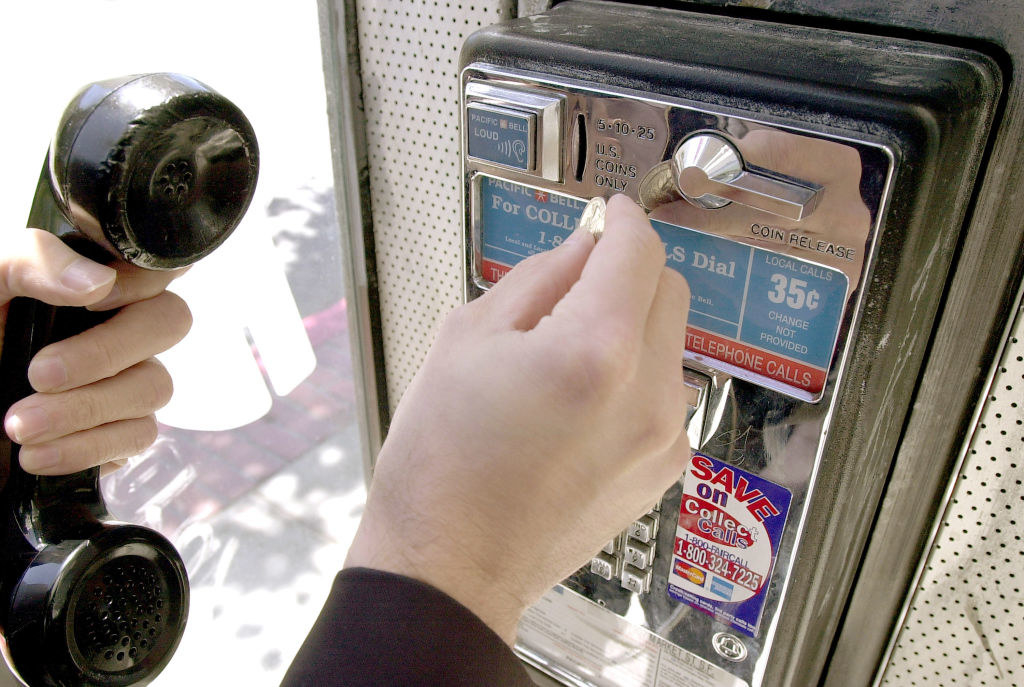 A hand holding the receiver and putting a quarter into the payphone 