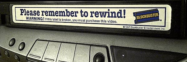 Blockbuster VHS tape with the sticker &quot;Please remember to rewind&quot; sticking out of the VCR