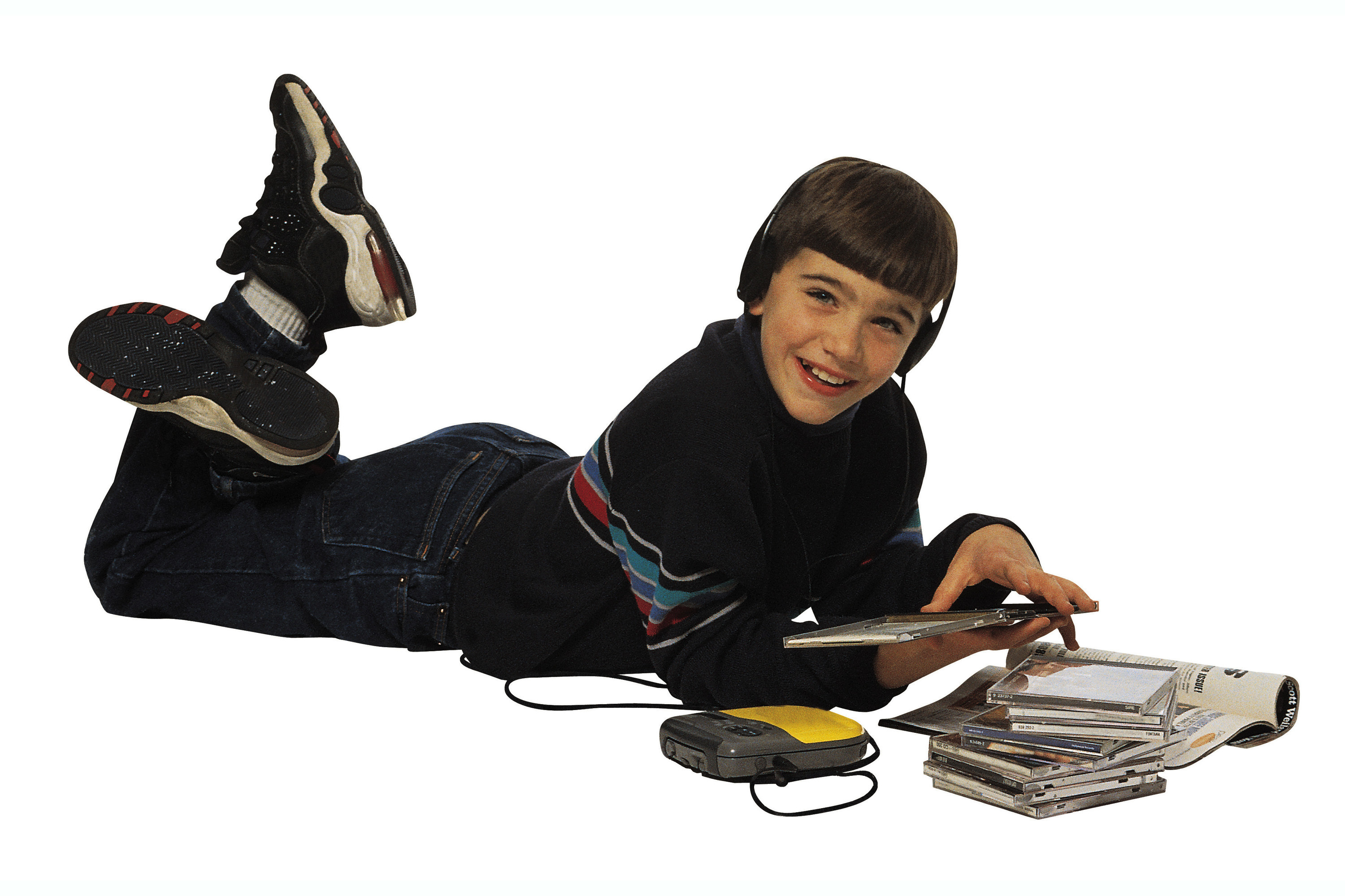 A &#x27;90s kids lying on the floor listening to a CD from his portable CD player while he has a CD case opened in his hand and has a stack of CDs next to him