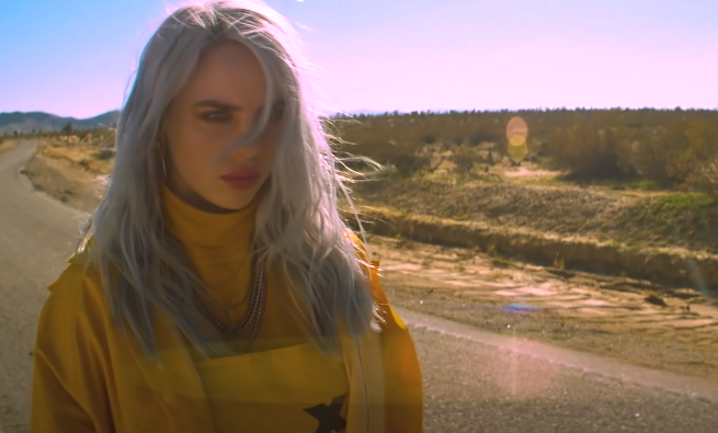 Billie Eilish standing in the middle of an empty road in the &quot;Bellyache&quot; music video