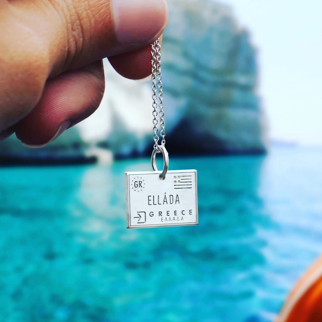 model holding up silver necklace pendant labeled &quot;Elláda Greece&quot; 