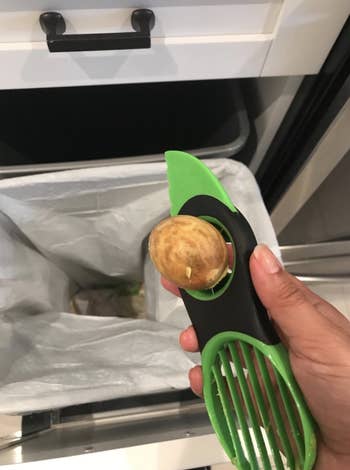 Reviewer using the tool to pit the avocado. The avocado is stuck to the tool with a hole for a finger to easily pop it out.