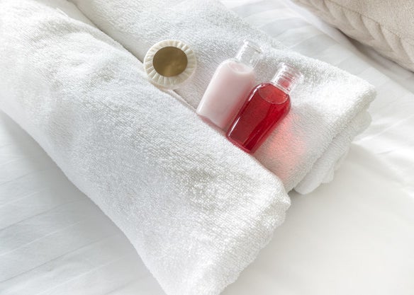 Colorful toiletry bottles and a wrapped up soap sit delicately on freshly rolled towels
