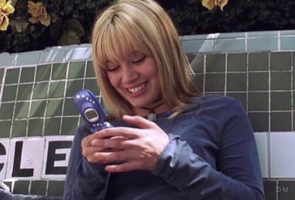 A screenshot of Lizzie McGuire texting on a blue flip phone 