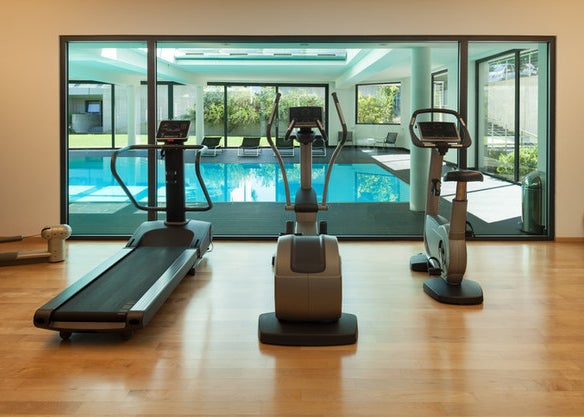 A modern looking gym made of three cardio machines facing a huge window overlooking an indoor pool