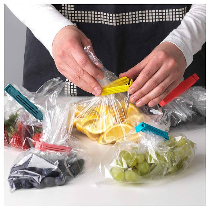 A person&#x27;s hand using the baggie seals to clip a clear plastic bag of lemons, surrounded by already sealed bags of several fruits.