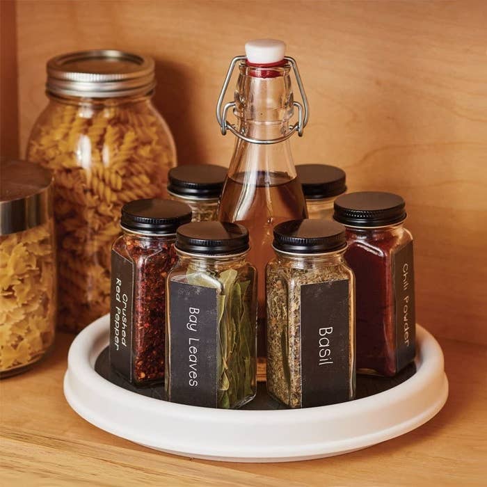 inside a kitchen cabinet with a clear lazy susan turntable containing jars of various spices within reach