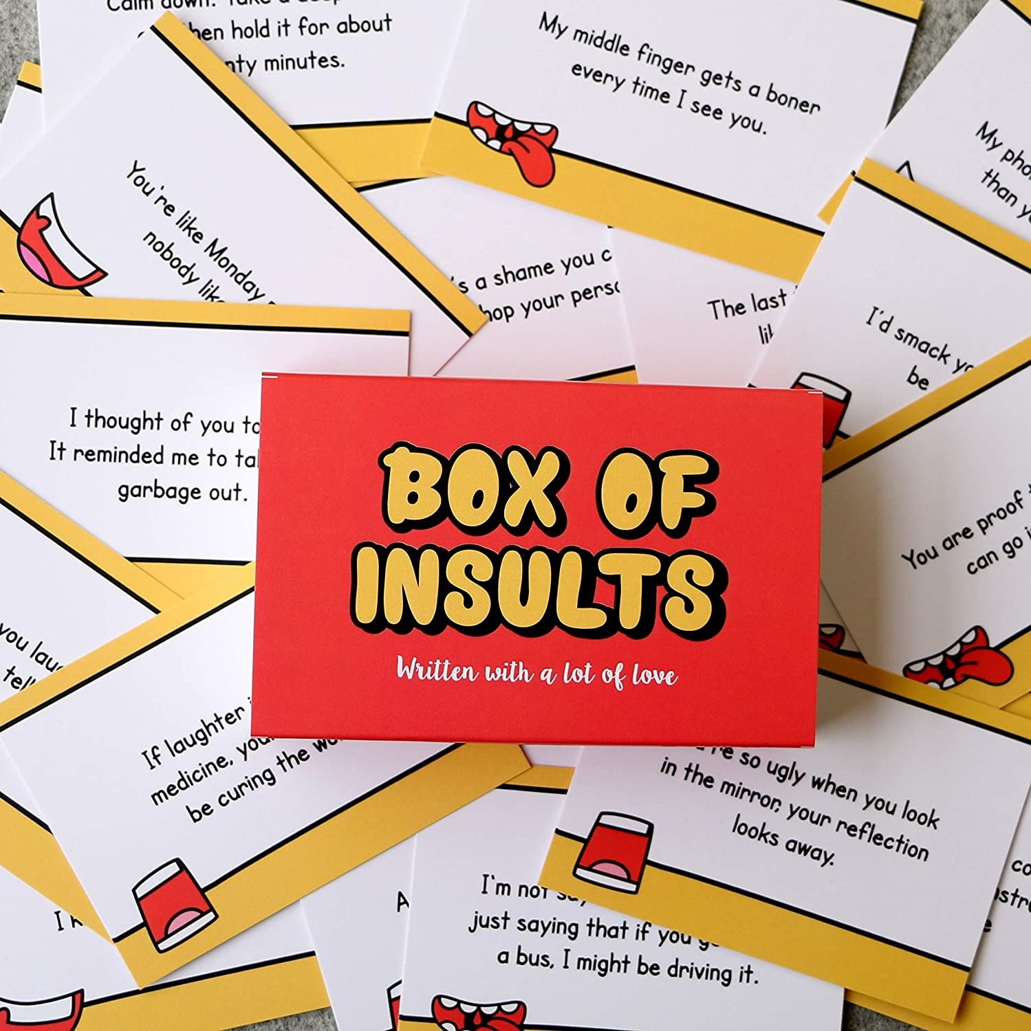 A box of insults kept over a background of different insulting cards, reading things like &quot;You&#x27;re so ugly when you look in the mirror, your reflection looks away.&quot;