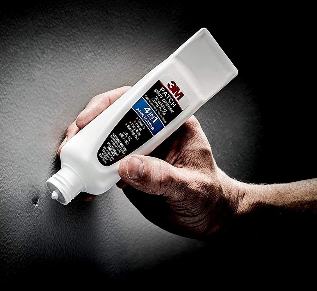 Model&#x27;s hand holding a white tube of spackle to patch a hole in the wall