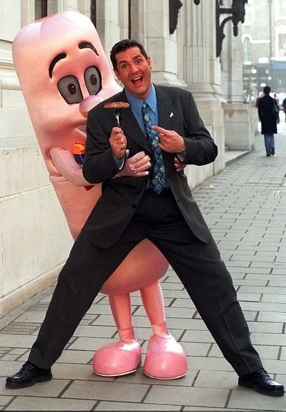man being hugged by man wearing a sausage costume.