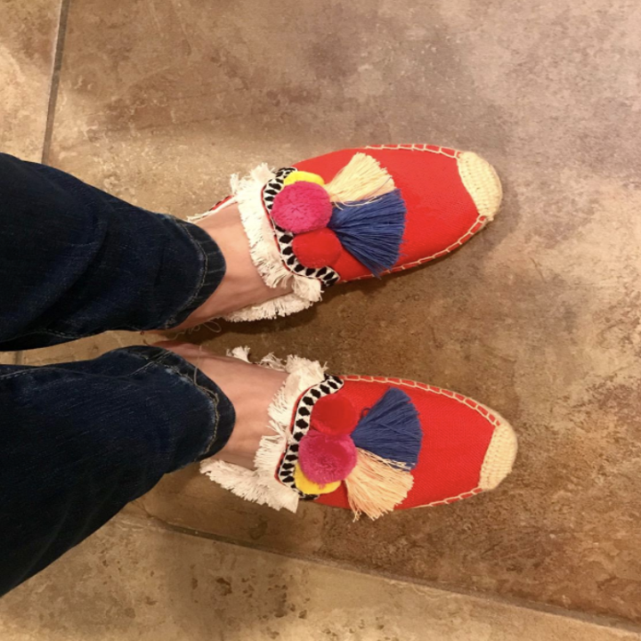 a reviewer wearing the shoes in red with pink, yellow, blue, and tan tassels