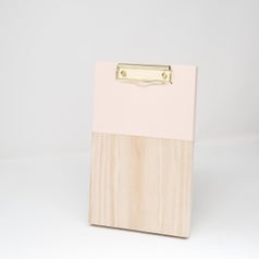 the clip board with a gold clip at the top, a pink top half, and a wooden bottom half