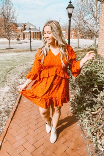 A reviewer wearing the dress in orange with white polka dots with taupe booties