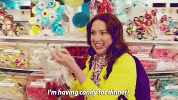 Kimmy from Unbreakable Kimmy Schmidt in a candy shop saying &quot;I&#x27;m having candy for dinner&quot;