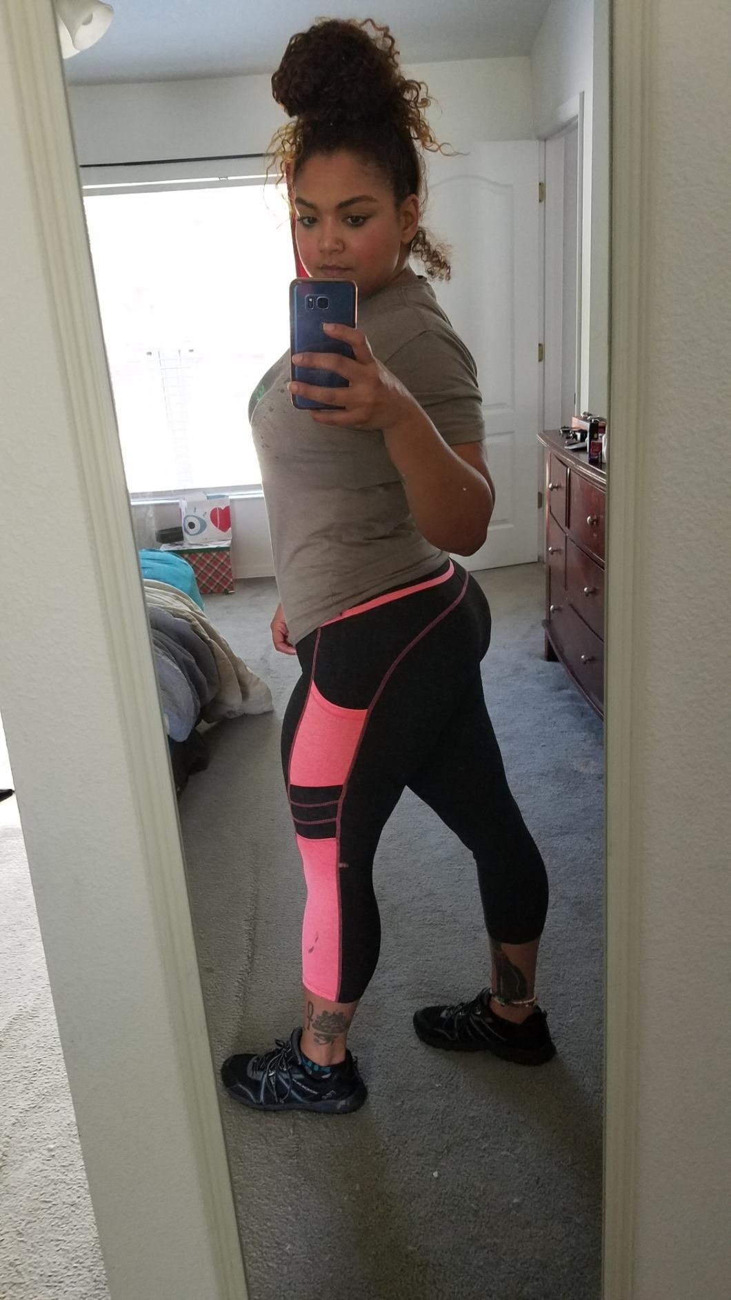 Reviewer wearing the calf-length leggings with pink stripe down the side with a pocket in the middle of it.