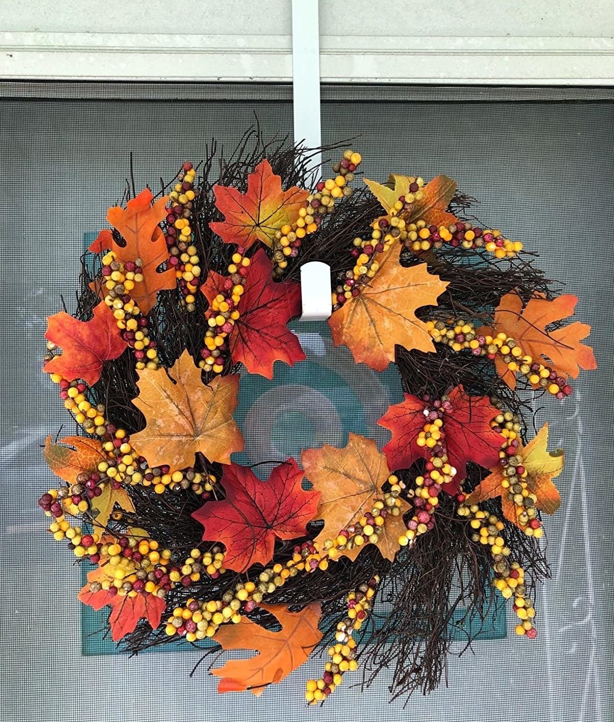 The wreath is full of colorful artificial maple leaves and berries and brown sticks 