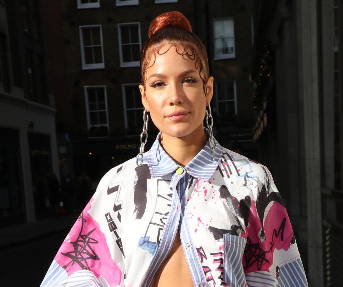 Halsey posing in a nearly-opened button-up shirt, chainlink earrings, a high bun