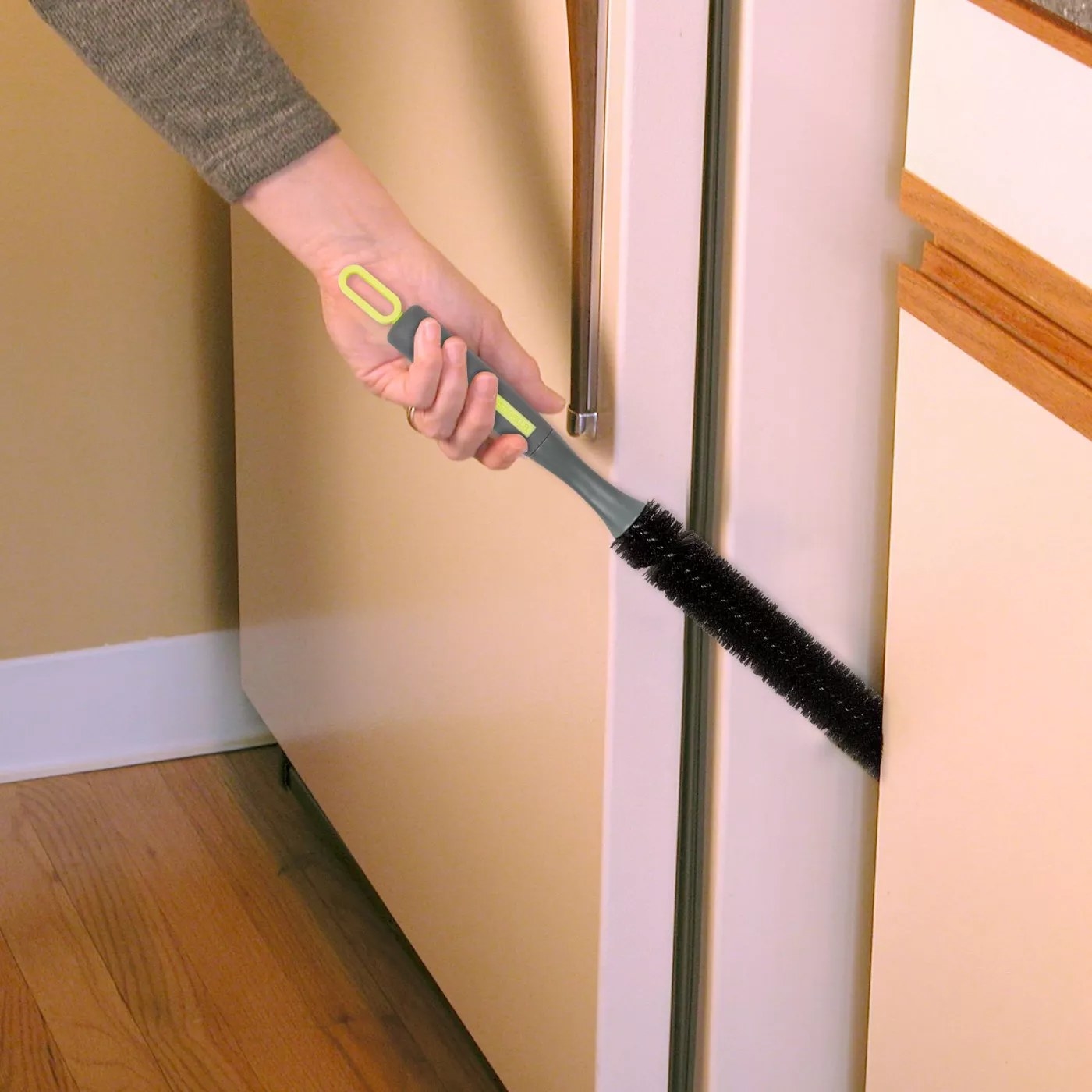 A model using a long bristle brush to clean in the space between the refrigerator and the cabinets