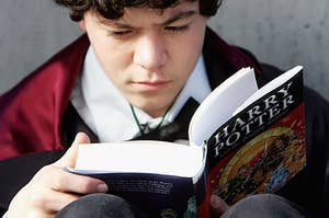 A young boy reads Harry Potter in a Hogwarts uniform