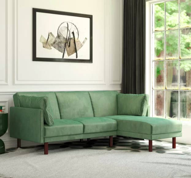 Velvet green sectional couch against a white wall with a painting above it