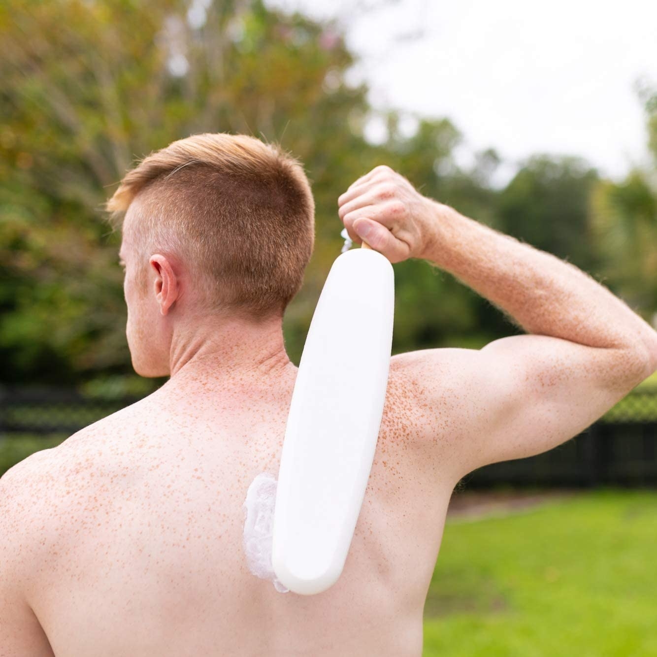 A person uses an applicator to spread a cream on their back