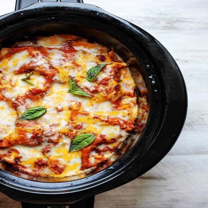 A slow cooker filled with cheesy eggplant lasagna topped with basil.