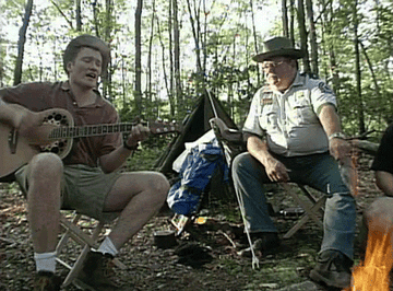 A gif of Conan O&#x27;Brien playing the guitar next to a campfire.